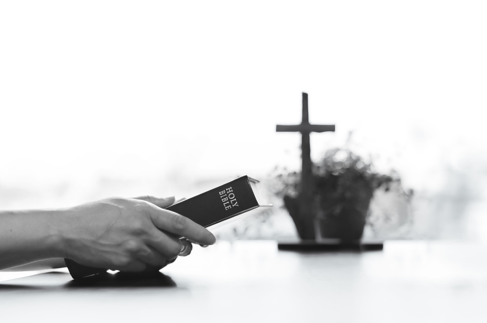 Christian praying and worshiping with holy bible in hand, cross of Jesus Christ in the background